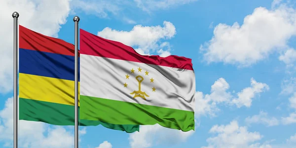 Bandera de Mauricio y Tayikistán ondeando en el viento contra el cielo azul nublado blanco juntos. Concepto diplomático, relaciones internacionales . — Foto de Stock