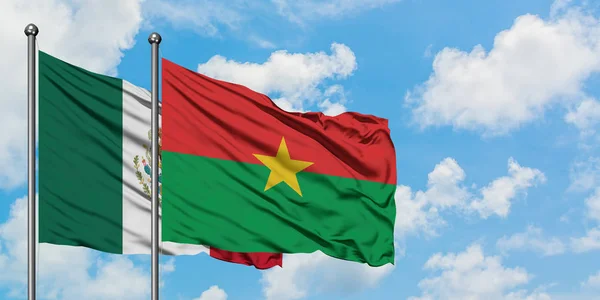 Bandera de México y Burkina Faso ondeando en el viento contra el cielo azul nublado blanco juntos. Concepto diplomático, relaciones internacionales . — Foto de Stock