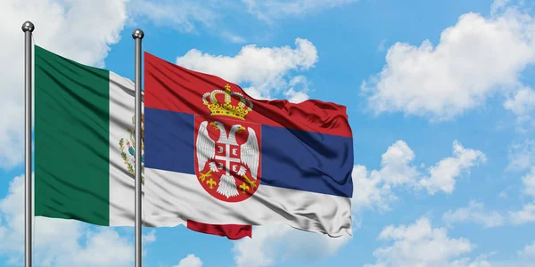 Bandera de México y Serbia ondeando en el viento contra el cielo azul nublado blanco juntos. Concepto diplomático, relaciones internacionales . — Foto de Stock