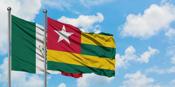Messico e Togo sventolano nel vento contro il bianco cielo blu nuvoloso insieme. Concetto di diplomazia, relazioni internazionali . — Foto Stock