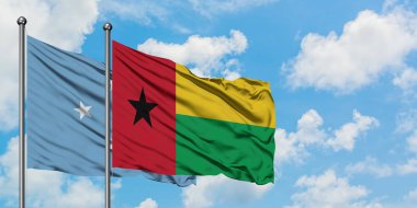 Mikronezya ve Gine Bissau bayrağı birlikte beyaz bulutlu mavi gökyüzüne karşı rüzgarda sallayarak. Diplomasi kavramı, uluslararası ilişkiler.