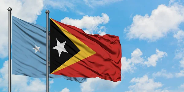 Micronesia y la bandera de Timor Oriental ondeando en el viento contra el cielo azul nublado blanco juntos. Concepto diplomático, relaciones internacionales . — Foto de Stock