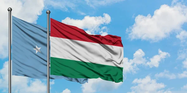Bandera de Micronesia y Hungría ondeando en el viento contra el cielo azul nublado blanco juntos. Concepto diplomático, relaciones internacionales . — Foto de Stock