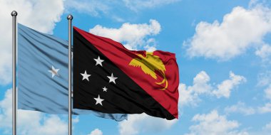 Mikronezya ve Papua Yeni Gine bayrağı birlikte beyaz bulutlu mavi gökyüzüne karşı rüzgarda sallayarak. Diplomasi kavramı, uluslararası ilişkiler.