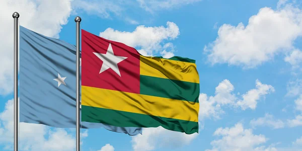 Micronesia y la bandera de Togo ondeando en el viento contra el cielo azul nublado blanco juntos. Concepto diplomático, relaciones internacionales . — Foto de Stock