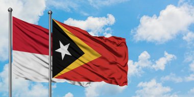 Monako ve Doğu Timor bayrağı birlikte beyaz bulutlu mavi gökyüzüne karşı rüzgarsal sallayarak. Diplomasi kavramı, uluslararası ilişkiler.