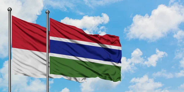 Monaco- und Gambia-Flagge wehen gemeinsam im Wind vor dem wolkenverhangenen blauen Himmel. Diplomatie-Konzept, internationale Beziehungen. — Stockfoto