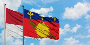 Monako ve Guadeloupe bayrağı birlikte beyaz bulutlu mavi gökyüzüne karşı rüzgarda sallayarak. Diplomasi kavramı, uluslararası ilişkiler.