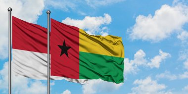 Monako ve Gine Bissau bayrağı birlikte beyaz bulutlu mavi gökyüzüne karşı rüzgarda sallayarak. Diplomasi kavramı, uluslararası ilişkiler.