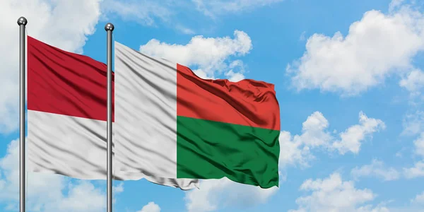 Drapeau de Monaco et Madagascar agitant dans le vent contre ciel bleu nuageux blanc ensemble. Concept de diplomatie, relations internationales . — Photo