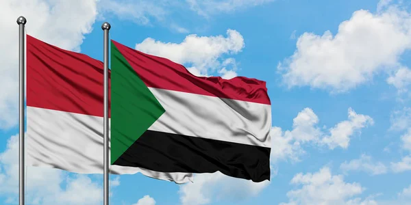 Monako a Súdánská vlajka mávali ve větru proti bíle zatažené modré obloze. Diplomacie, mezinárodní vztahy. — Stock fotografie