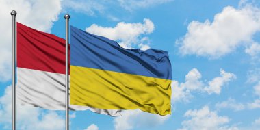 Monako ve Ukrayna bayrağı birlikte beyaz bulutlu mavi gökyüzüne karşı rüzgarda sallayarak. Diplomasi kavramı, uluslararası ilişkiler.