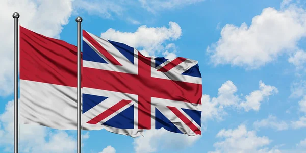 Monaco och Storbritannien flagga vifta i vinden mot vit grumlig blå himmel tillsammans. Diplomatisk koncept, internationella relationer. — Stockfoto