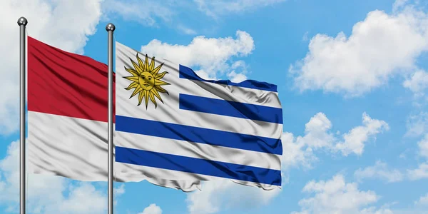 Bandera de Mónaco y Uruguay ondeando en el viento contra el cielo azul nublado blanco juntos. Concepto diplomático, relaciones internacionales . —  Fotos de Stock