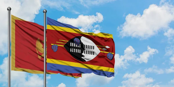 Montenegro y la bandera de Suazilandia ondeando en el viento contra el cielo azul nublado blanco juntos. Concepto diplomático, relaciones internacionales . — Foto de Stock