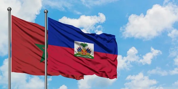 Marrocos e a bandeira do Haiti agitando no vento contra o céu azul nublado branco juntos. Conceito de diplomacia, relações internacionais . — Fotografia de Stock