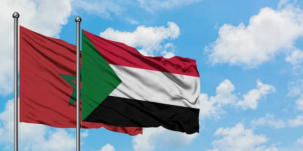Bandera de Marruecos y Sudán ondeando en el viento contra el cielo azul nublado blanco juntos. Concepto diplomático, relaciones internacionales . — Foto de Stock