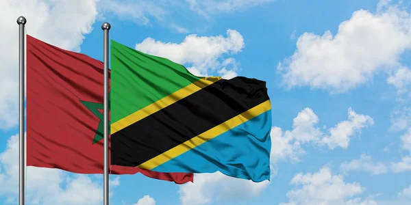 Bandera de Marruecos y Tanzania ondeando en el viento contra el cielo azul nublado blanco juntos. Concepto diplomático, relaciones internacionales . — Foto de Stock