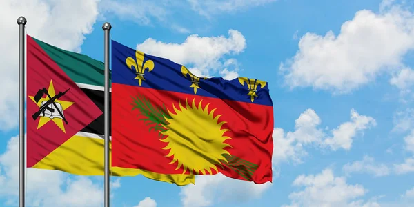 Bandera de Mozambique y Guadalupe ondeando en el viento contra el cielo azul nublado blanco juntos. Concepto diplomático, relaciones internacionales . — Foto de Stock