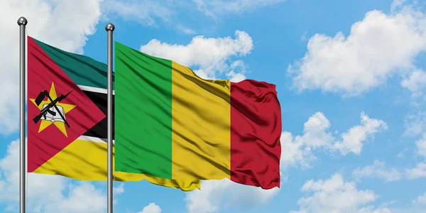 Moçambique e a bandeira do Mali agitando no vento contra o céu azul nublado branco juntos. Conceito de diplomacia, relações internacionais . — Fotografia de Stock
