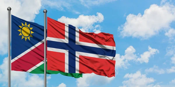 Bandera de Namibia y Bouvet Islands ondeando en el viento contra el cielo azul nublado blanco juntos. Concepto diplomático, relaciones internacionales . — Foto de Stock