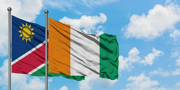 Vlag van Namibië en Ivoorkust zwaaiende in de wind tegen witte bewolkte blauwe hemel samen. Diplomatie concept, internationale betrekkingen. — Stockfoto