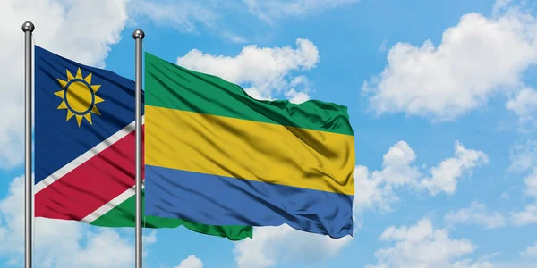 Drapeau de Namibie et du Gabon agitant dans le vent contre ciel bleu nuageux blanc ensemble. Concept de diplomatie, relations internationales . — Photo