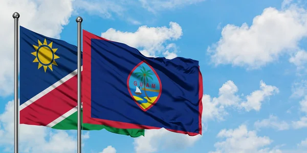Bandera de Namibia y Guam ondeando en el viento contra el cielo azul nublado blanco juntos. Concepto diplomático, relaciones internacionales . — Foto de Stock