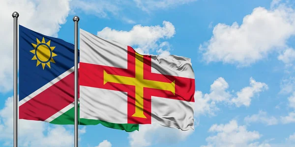 Namibya ve Guernsey bayrağı birlikte beyaz bulutlu mavi gökyüzüne karşı rüzgarda sallayarak. Diplomasi kavramı, uluslararası ilişkiler. — Stok fotoğraf