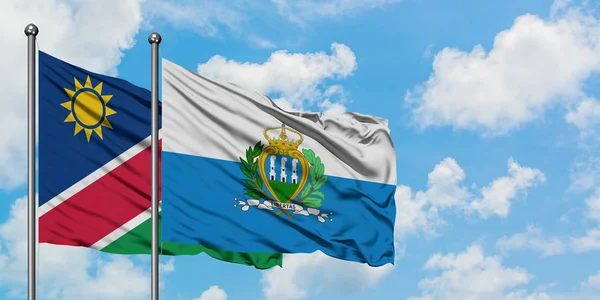 Namibia y la bandera de San Marino ondeando en el viento contra el cielo azul nublado blanco juntos. Concepto diplomático, relaciones internacionales . — Foto de Stock