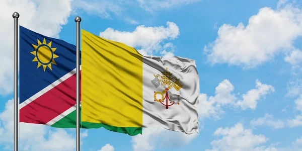 Namibie et le drapeau de la Cité du Vatican agitant dans le vent contre ciel bleu nuageux blanc ensemble. Concept de diplomatie, relations internationales . — Photo
