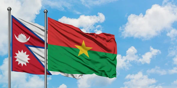 Bandera de Nepal y Burkina Faso ondeando en el viento contra el cielo azul nublado blanco juntos. Concepto diplomático, relaciones internacionales . — Foto de Stock