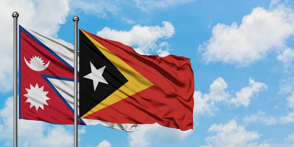 Bandera de Nepal y Timor Oriental ondeando en el viento contra el cielo azul nublado blanco juntos. Concepto diplomático, relaciones internacionales . — Foto de Stock