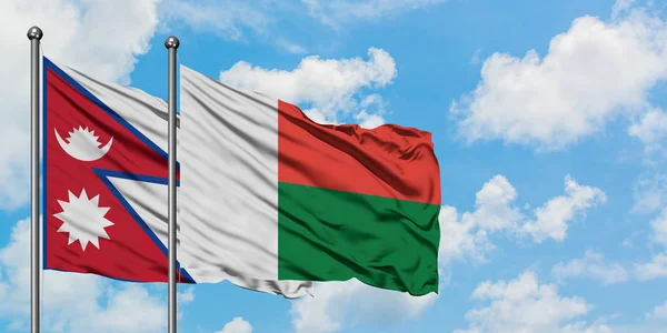 Bandera de Nepal y Madagascar ondeando en el viento contra el cielo azul nublado blanco juntos. Concepto diplomático, relaciones internacionales . — Foto de Stock