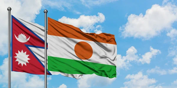 Bandera de Nepal y Níger ondeando en el viento contra el cielo azul nublado blanco juntos. Concepto diplomático, relaciones internacionales . — Foto de Stock