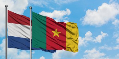 Hollanda ve Kamerun bayrağı birlikte beyaz bulutlu mavi gökyüzüne karşı rüzgarsal sallayarak. Diplomasi kavramı, uluslararası ilişkiler.