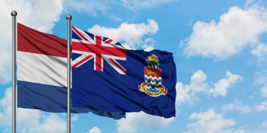 Hollanda ve Cayman Adaları bayrağı birlikte beyaz bulutlu mavi gökyüzüne karşı rüzgarsal sallayarak. Diplomasi kavramı, uluslararası ilişkiler.