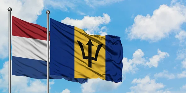 Bandera de Holanda y Barbados ondeando en el viento contra el cielo azul nublado blanco juntos. Concepto diplomático, relaciones internacionales . — Foto de Stock