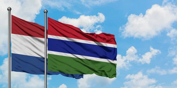 Niederlande und Gambia schwenken gemeinsam die Flagge im Wind gegen den wolkenverhangenen blauen Himmel. Diplomatie-Konzept, internationale Beziehungen. — Stockfoto