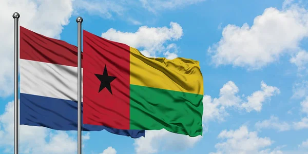 Holanda e Guiné-Bissau acenando com o vento contra o céu azul nublado branco juntos. Conceito de diplomacia, relações internacionais . — Fotografia de Stock
