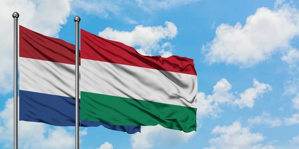Bandera de Holanda y Hungría ondeando en el viento contra el cielo azul nublado blanco juntos. Concepto diplomático, relaciones internacionales . — Foto de Stock