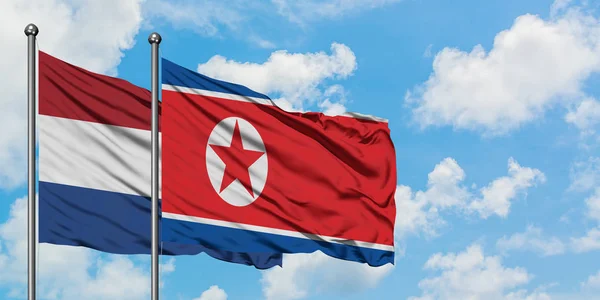 Holanda e Coreia do Norte acenando com o vento contra o céu azul nublado branco juntos. Conceito de diplomacia, relações internacionais . — Fotografia de Stock