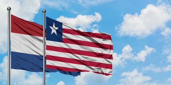 Bandera de Holanda y Liberia ondeando en el viento contra el cielo azul nublado blanco juntos. Concepto diplomático, relaciones internacionales . — Foto de Stock