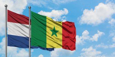 Hollanda ve Senegal bayrağı birlikte beyaz bulutlu mavi gökyüzüne karşı rüzgarsal sallayarak. Diplomasi kavramı, uluslararası ilişkiler.