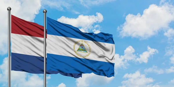 Bandera de Holanda y Nicaragua ondeando en el viento contra el cielo azul nublado blanco juntos. Concepto diplomático, relaciones internacionales . —  Fotos de Stock