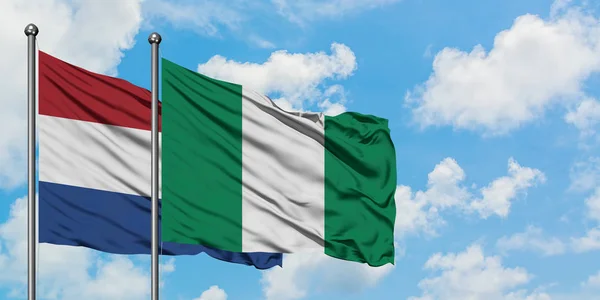 Paesi Bassi e Nigeria bandiera sventolando nel vento contro bianco cielo blu nuvoloso insieme. Concetto di diplomazia, relazioni internazionali . — Foto Stock