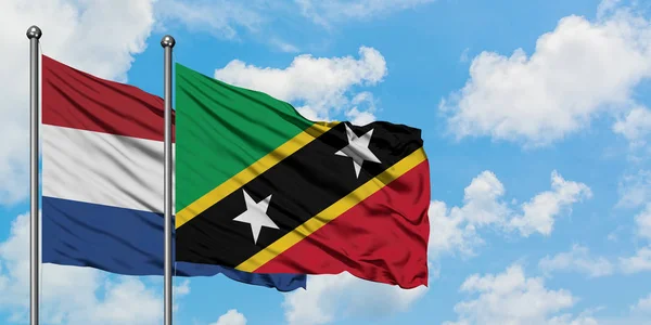 Nederländerna och Saint Kitts och Nevis flagga vifta i vinden mot vit grumlig blå himmel tillsammans. Diplomatisk koncept, internationella relationer. — Stockfoto