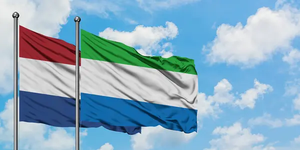 Paesi Bassi e Sierra Leone sventolano insieme la bandiera contro il bianco cielo azzurro nuvoloso. Concetto di diplomazia, relazioni internazionali . — Foto Stock