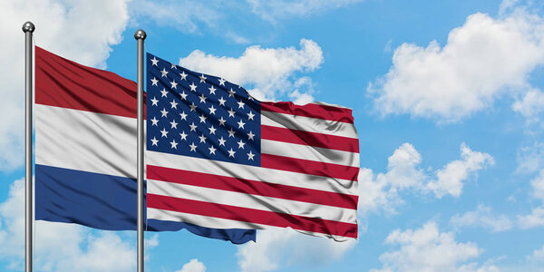 Netherlands and United States flag waving in the wind against white cloudy blue sky together. Diplomacy concept, international relations.