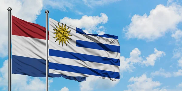 Η σημαία της Ολλανδίας και της Ουρουγουάης κουνώντας τον άνεμο εναντίον του λευκού νεφελώδη μπλε ουρανού μαζί. Φιλοσοφία της διπλωματίας, διεθνείς σχέσεις. — Φωτογραφία Αρχείου